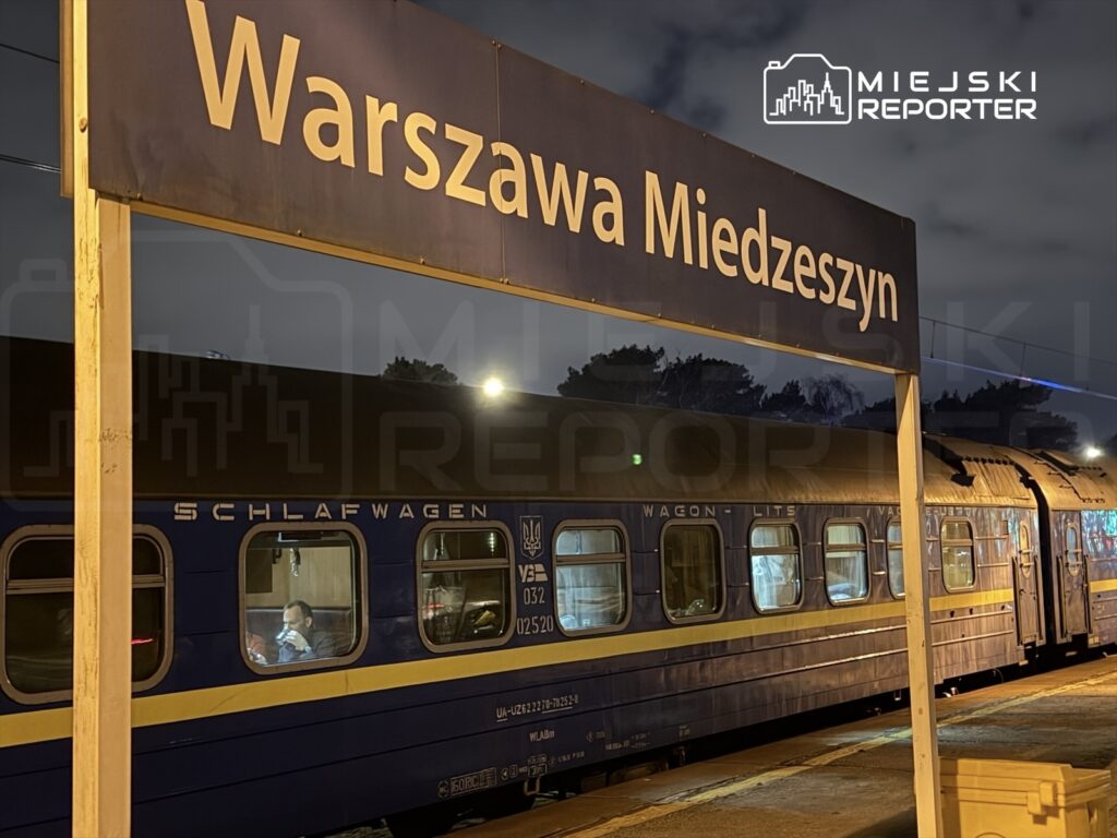 Pociąg sypialny zatrzymany na stacji Warszawa Miedzeszyn w nocy, pasażer korzystający z telefonu w oknie.