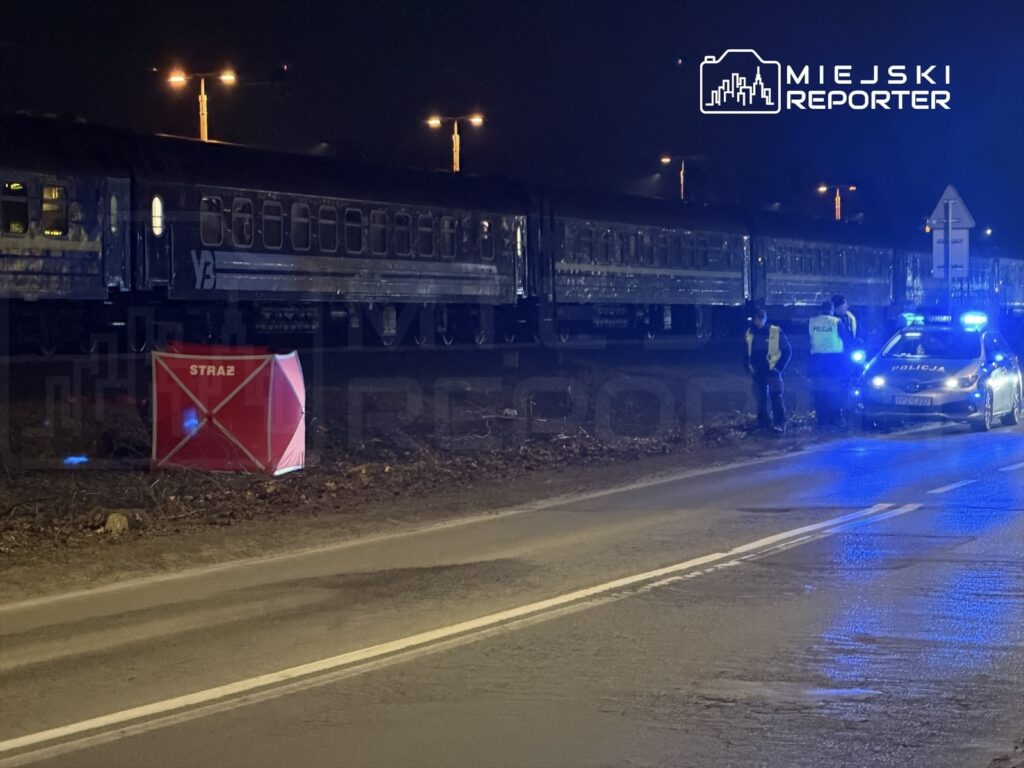 Grupa policjantów w odblaskowych kamizelkach prowadzi działania obok torów kolejowych w nocy, obok stoi radiowóz.