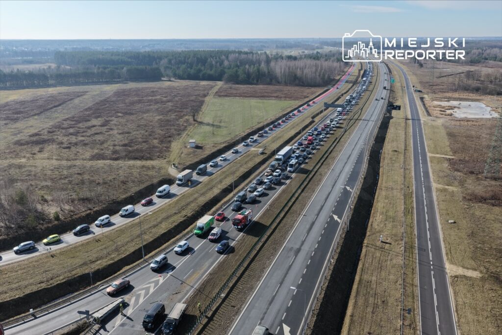 Ruch samochodowy w kierunku przeciwnym do zatoru na drodze, z długą kolejką pojazdów widoczną w tle.