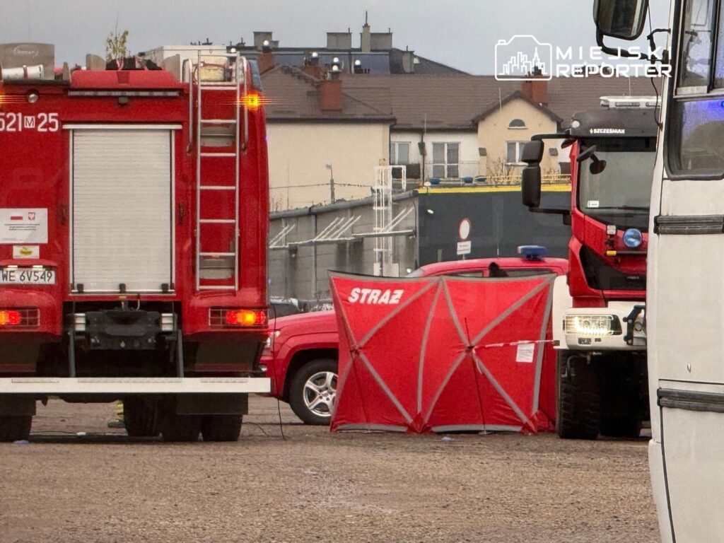 Czerwony wóz strażacki stoi obok zorganizowanego miejsca akcji ratunkowej z czerwonym namiotem z napisem "STRAŻ".
