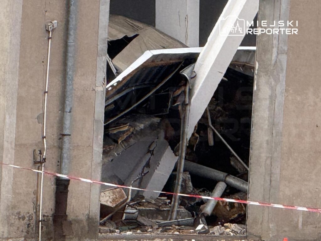 Uszkodzona ściana budynku z widocznymi zniszczeniami, odsłaniająca wnętrze i gruz w otoczeniu.