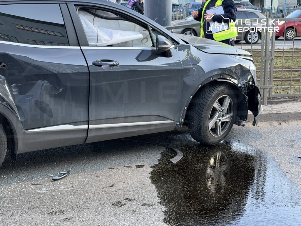 Uszkodzony samochód osobowy z wgniecioną karoserią stoi na jezdni, obok widoczna kałuża płynów eksploatacyjnych.
