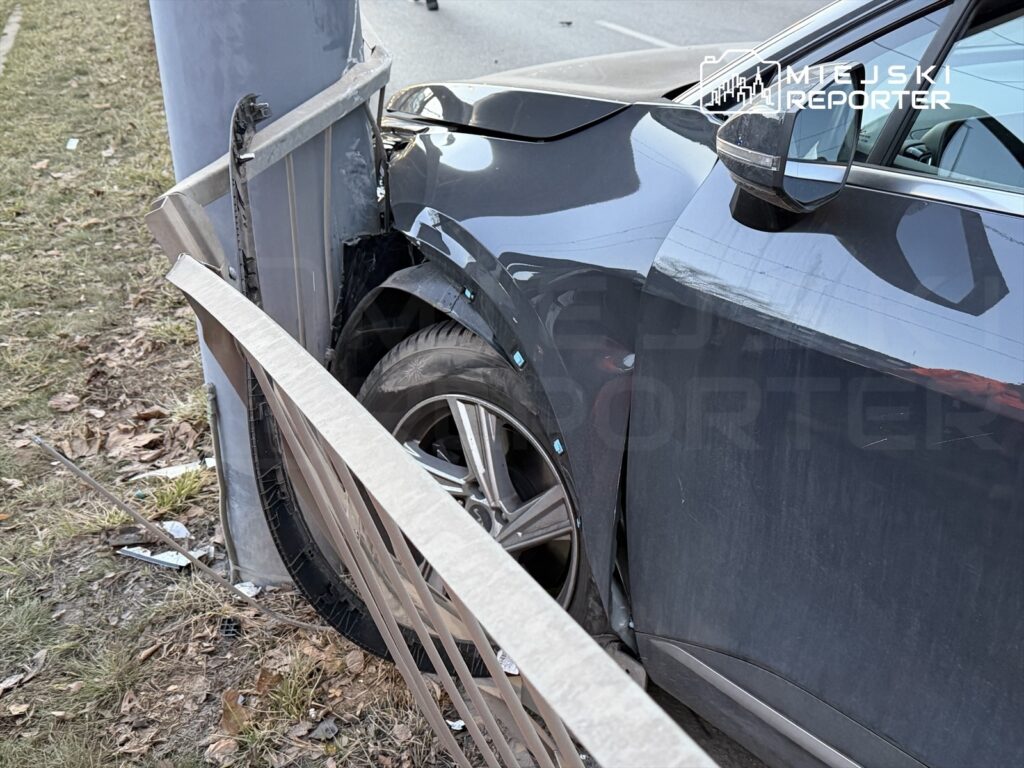 Czarny samochód osobowy uderzył w metalowy słup, zarysowując nadwozie i uszkadzając barierkę ochronną.