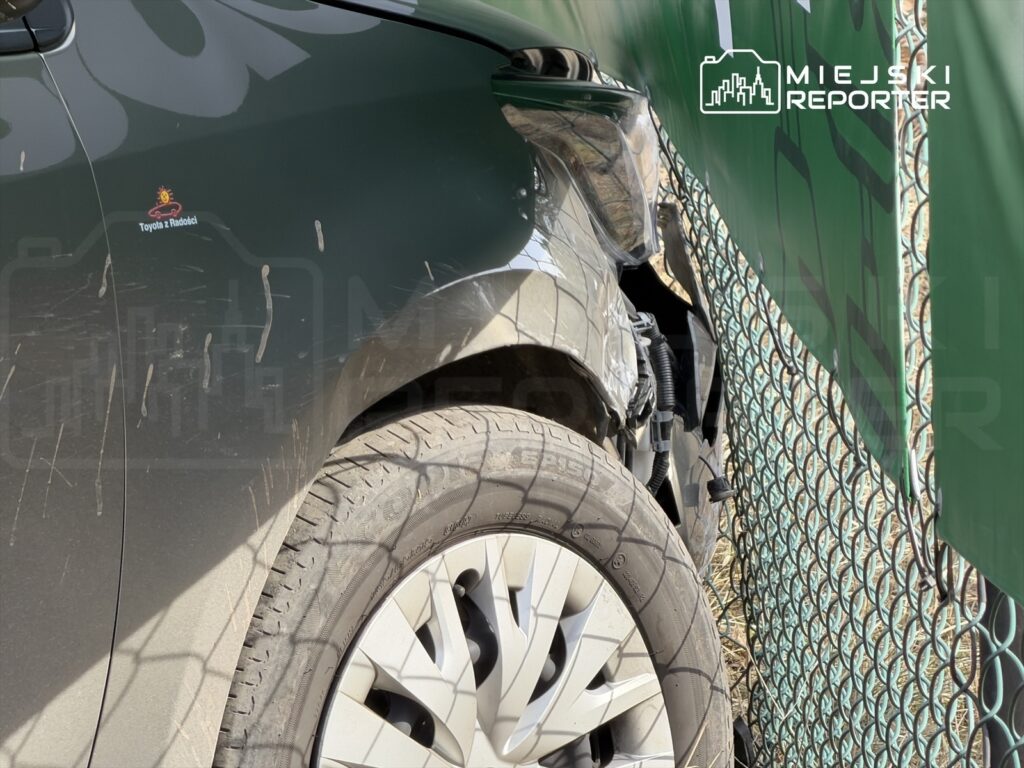 Zarysowany bok samochodu osobowego w pobliżu siatki ogrodzeniowej.