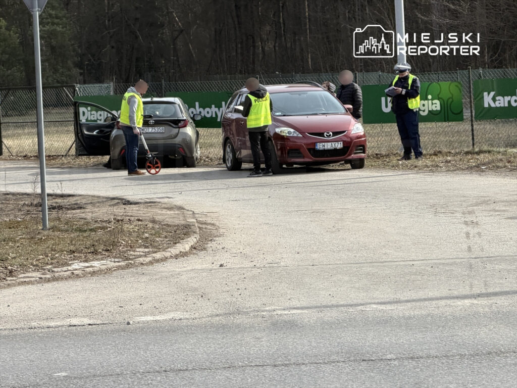 Grupa osób w odblaskowych kamizelkach mierzy odległość przy zaparkowanych samochodach na drodze.