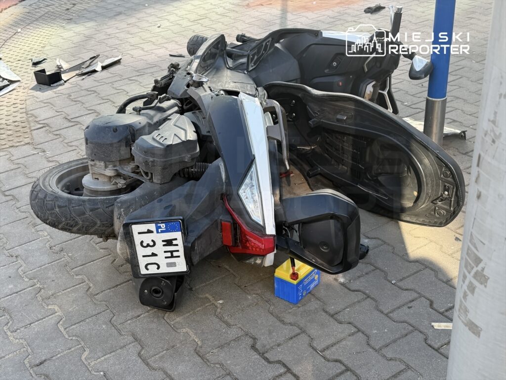 Przewrócony skuter leży na chodniku, obok niego znajduje się narzędzie i części.