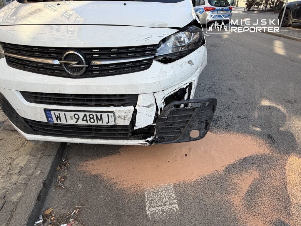 Biały samochód osobowy z uszkodzoną przednią częścią stoi na ulicy, obok widoczny plamisty ślad na jezdni.