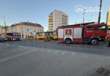 Strażacy prowadzą działania ratunkowe przy żółtym tramwaju w miejskim otoczeniu, obok zaparkowanych pojazdów.