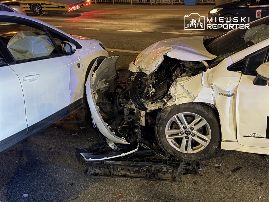 Dwa uszkodzone samochody osobowe zderzone na ulicy, widoczne zniszczenia przodu jednego z pojazdów.