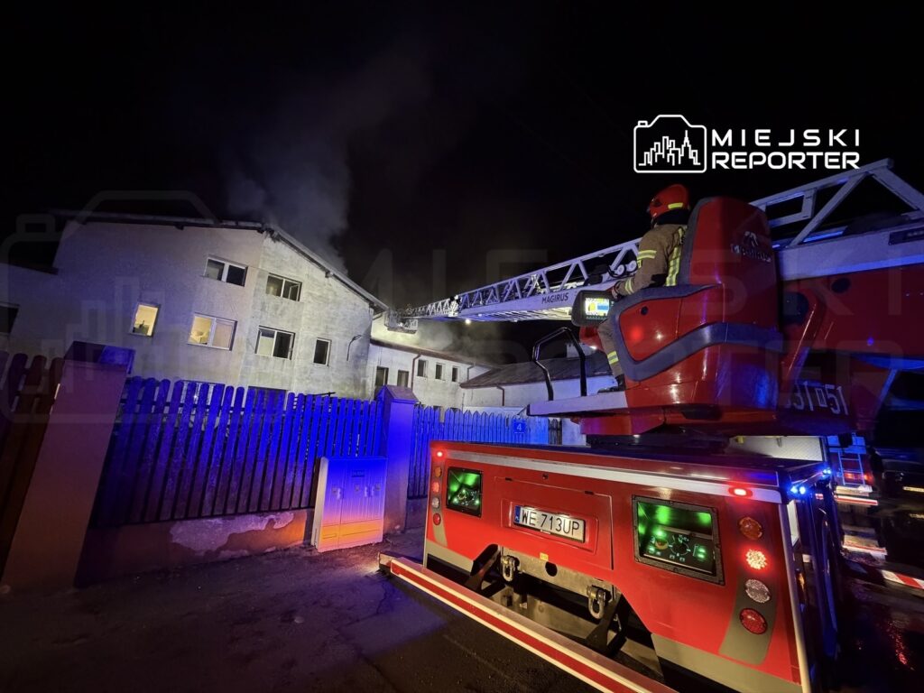 Strażak na podnośniku gaśniczym prowadzi akcję ratunkową przy budynku objętym pożarem w nocy.