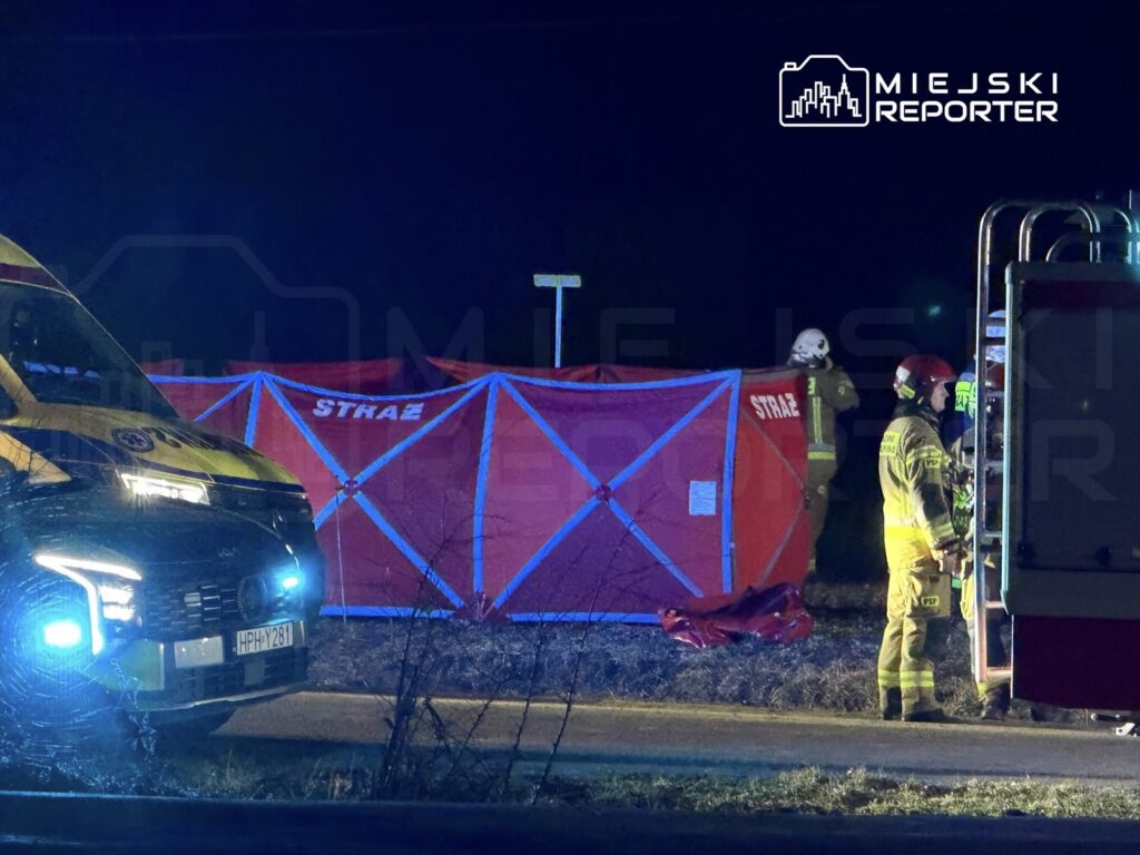 Zespół ratunkowy w mundurach pracuje w nocy przy oznakowanym namiocie strażackim obok karetki pogotowia.