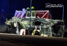 Zniszczony samochód leży na boku na drodze, a w tle widać strażaków pracujących przy oświetleniu awaryjnym.