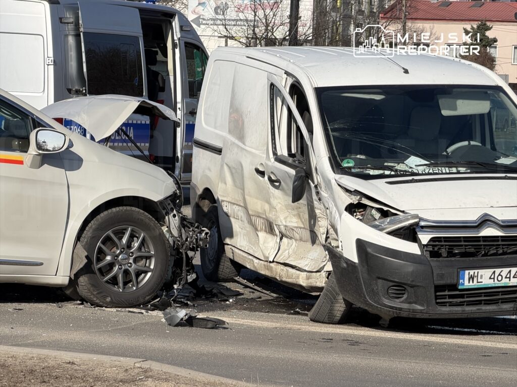Dwa uszkodzone samochody osobowe zderzone na drodze; biały van z wgniecioną stroną i szary pojazd z otwartą maską.