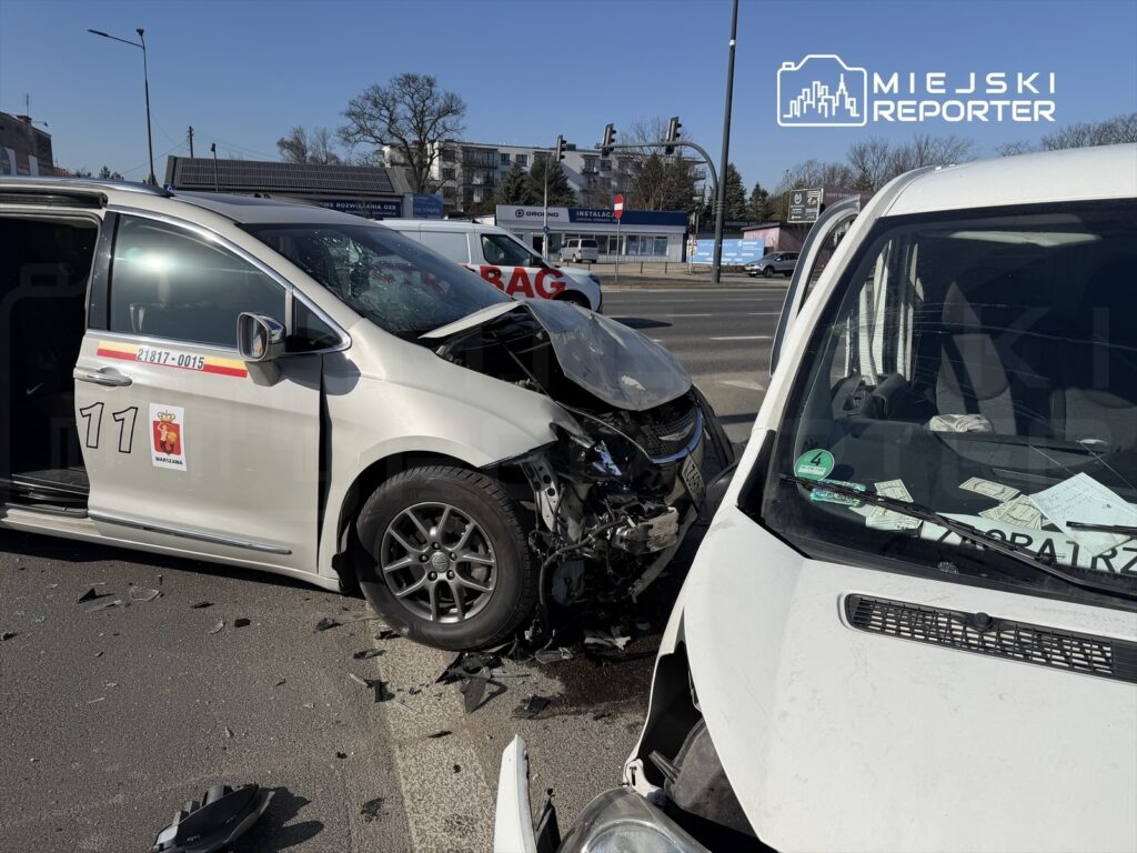 Dwa uszkodzone samochody osobowe po zderzeniu na ruchliwej ulicy, wokół rozbite szkło i wgniecione karoserie.