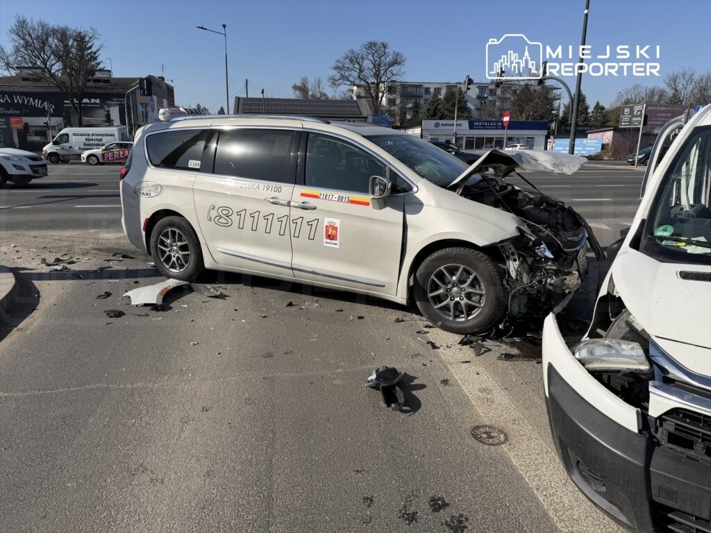 Zderzenie dwóch samochodów osobowych na ruchliwej ulicy, z uszkodzeniami przodu jednego z pojazdów.