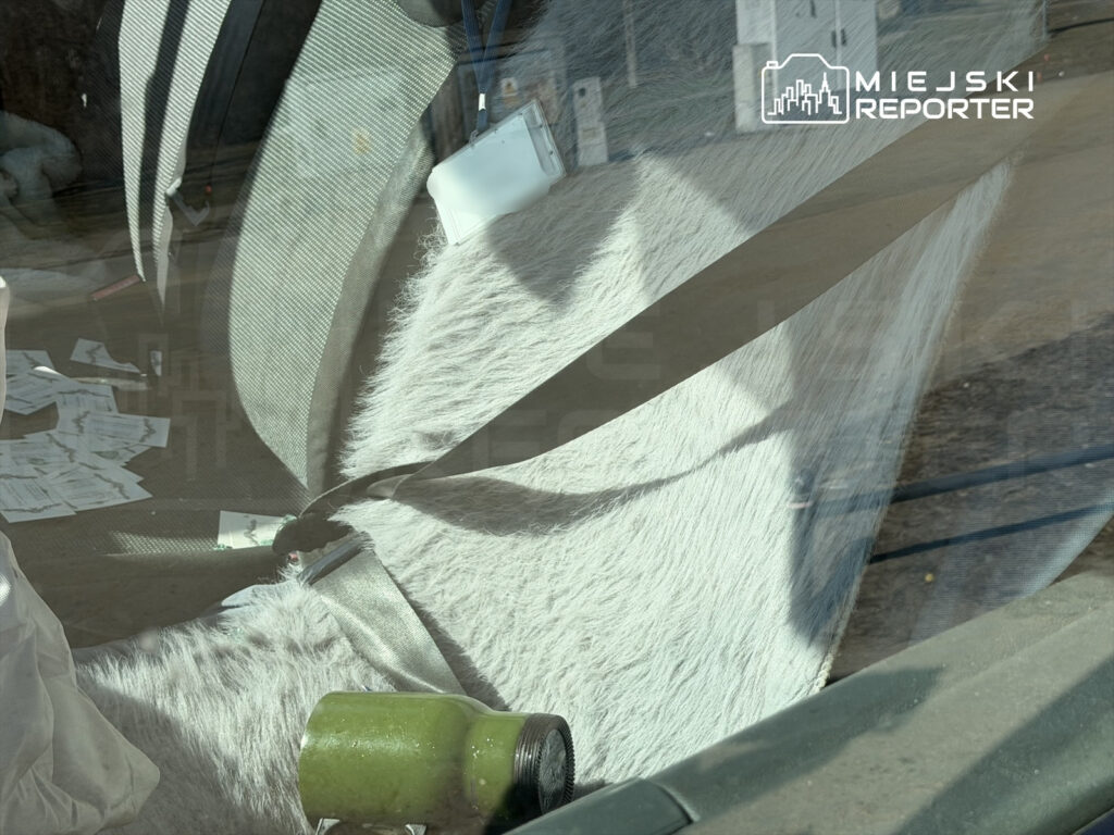 Wnętrze samochodu z białym futrem na siedzeniu, porozrzucane wizytówki i narzędzie na podłodze.