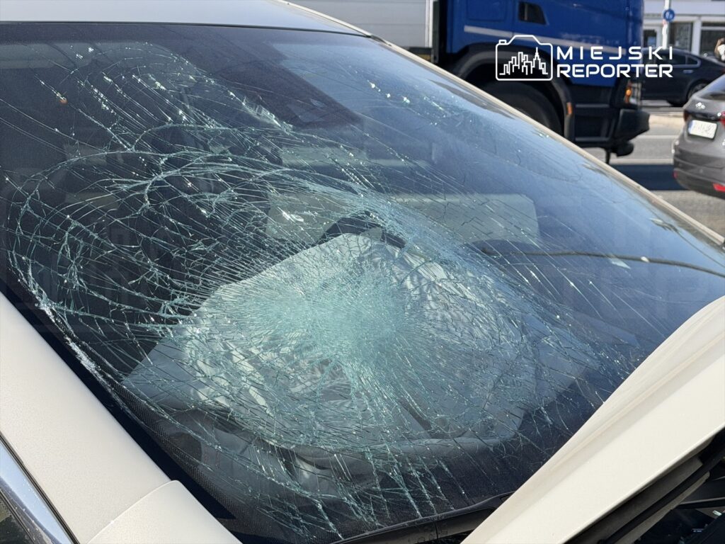 Pęknięta szyba przednia samochodu z wieloma spękaniami, stojącego na ruchliwej ulicy.