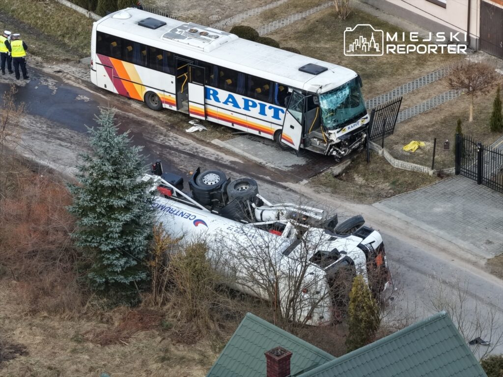 Wielki autobus przewoźnika "RAPIT" z uszkodzoną przednią częścią stoi obok przewróconego białego autobusu na drodze.