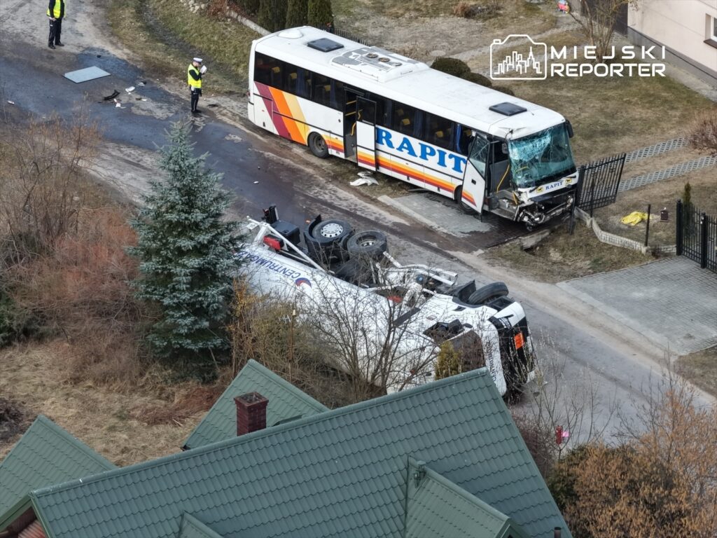 Dwa autobusy po wypadku na drodze, jeden przewrócony na bok, a drugi z uszkodzoną szybą, obok funkcjonariusze policji.