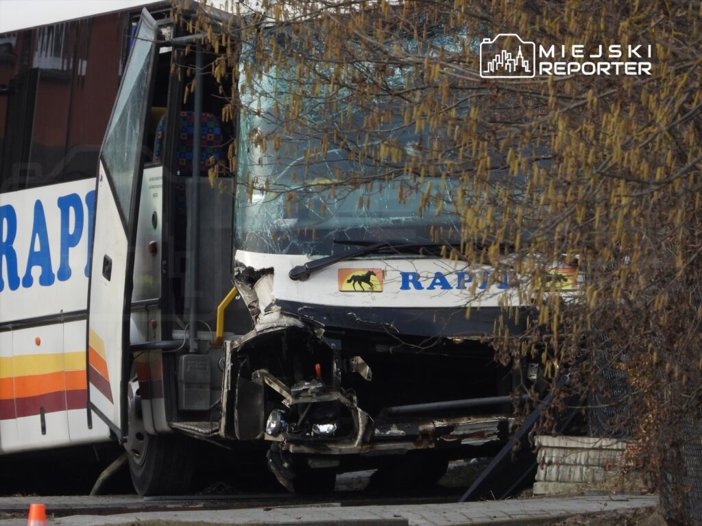 Zniszczony autobus z otwartymi drzwiami stoi obok drzewa, z widocznymi uszkodzeniami przodu.