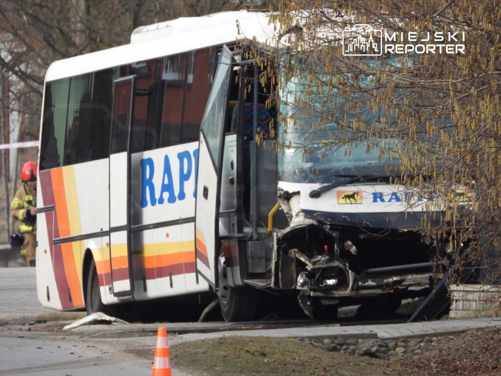 Autobus z widocznymi uszkodzeniami stoi na poboczu drogi, obok pracują strażacy w hełmach.