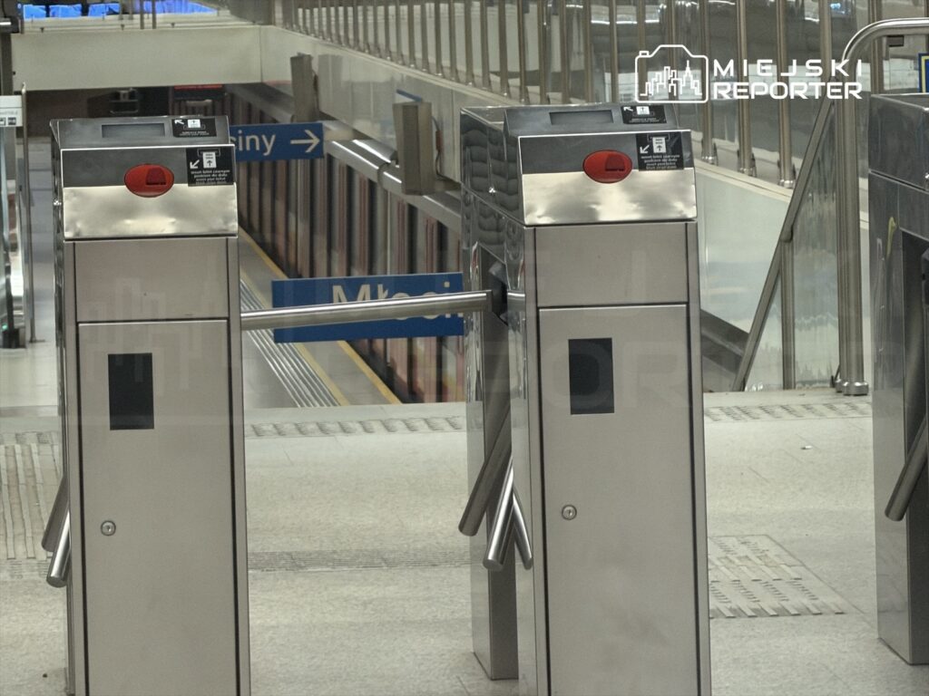 Dwa automaty biletowe na stacji metra, w tle widoczna platforma i kierunkowskaz do Młynów.