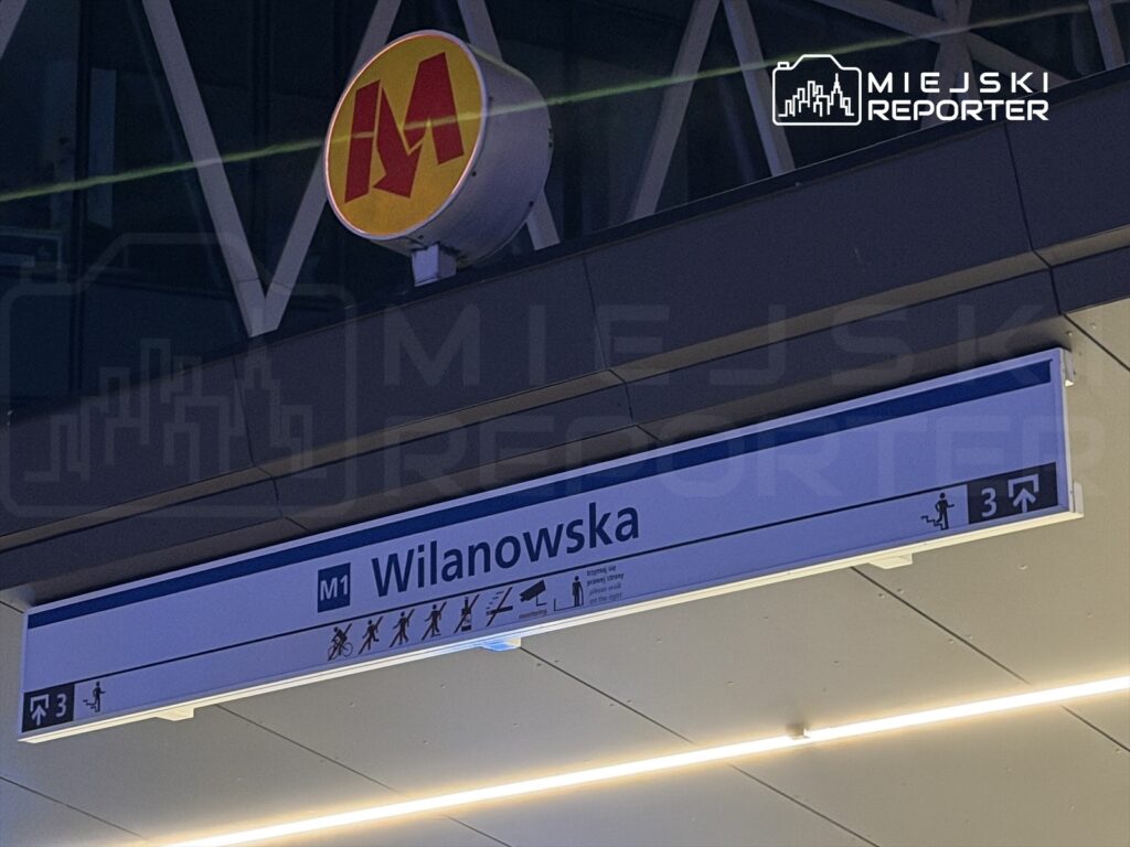 Znak stacji metra "Wilanowska" z informacjami o linii M1 oraz symbolami dla pasażerów.