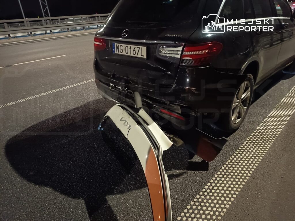 Uszkodzony tył czarnego SUV-a z odłączonym zderzakiem na nocnej jezdni.