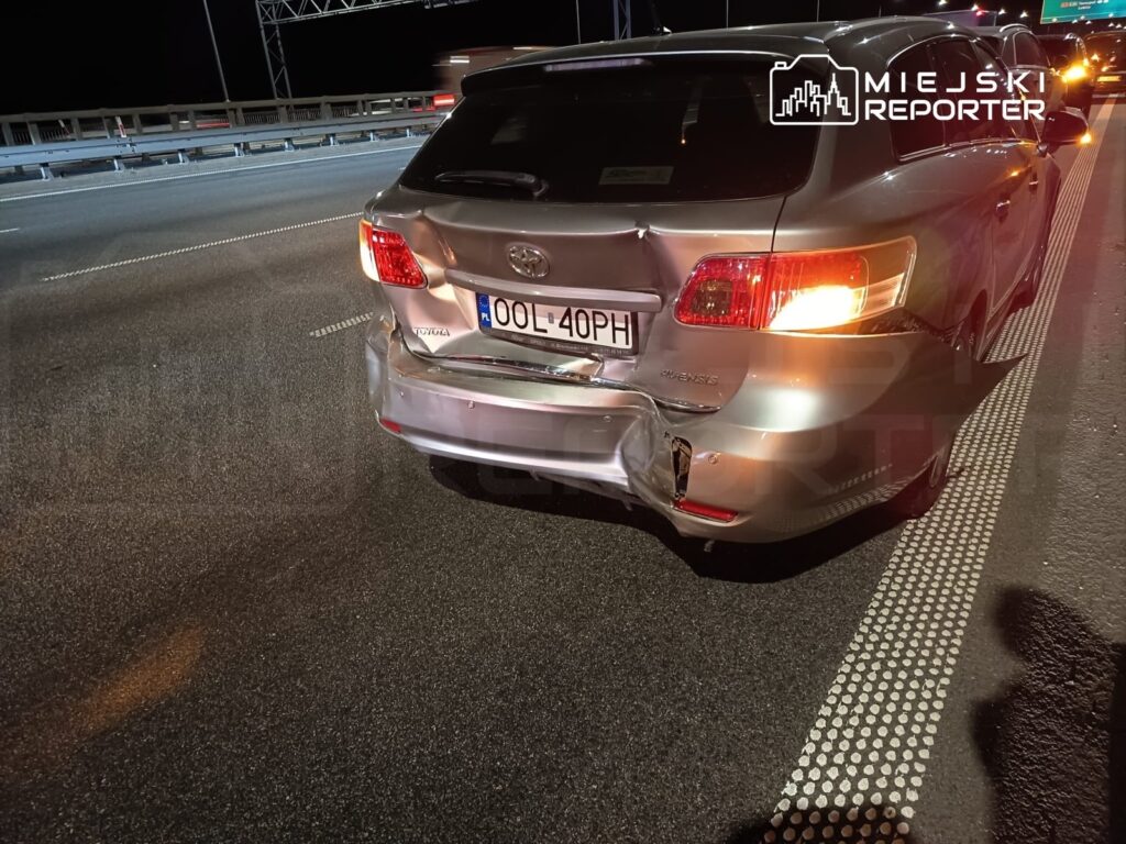 Uszkodzony samochód osobowy marki Toyota stojący na pasie drogowym w nocy, z widocznymi wgnieceniami z tyłu.