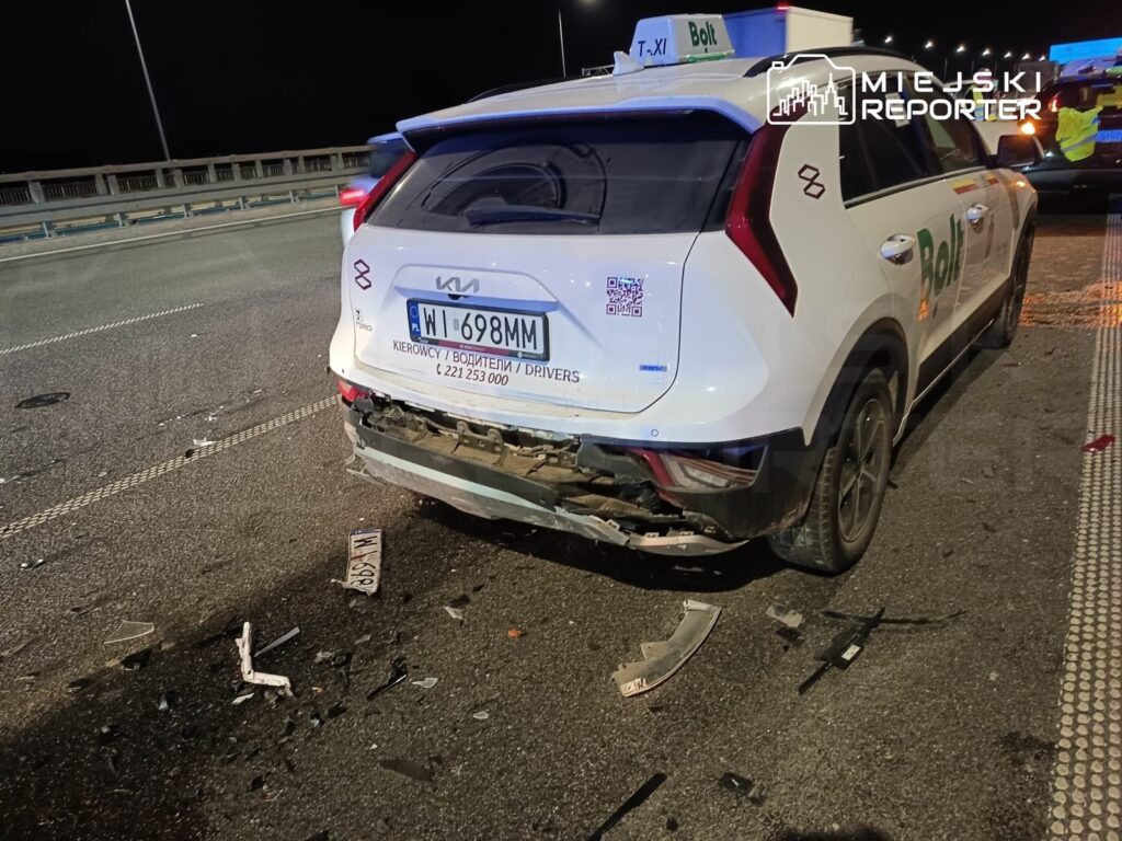 Uszkodzony samochód osobowy z widocznymi wgnieceniami na tylnej części stoi na drodze, obok leżą fragmenty zderzaka.