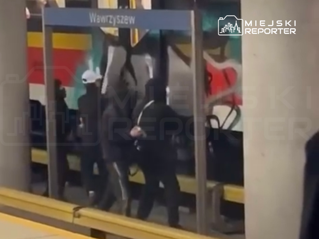 Grupa osób w ciemnych ubraniach wchodzi do pociągu na stacji Wawrzyszew, w tle kolorowy mural.