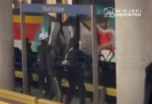 Grupa osób w ciemnych ubraniach wchodzi do pociągu na stacji Wawrzyszew, w tle kolorowy mural.