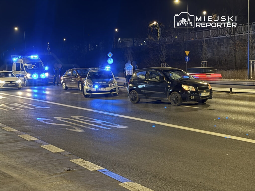 Na drodze zatrzymane są dwa pojazdy policyjne oraz jeden samochód cywilny, otoczone niebieskimi światłami w nocy.