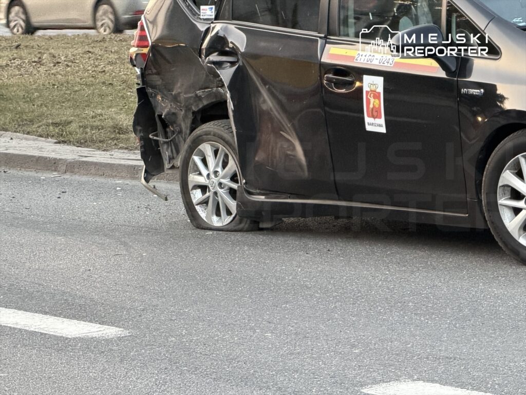 Czarny samochód osobowy z uszkodzeniem tyłu stoi na drodze obok trawnika.