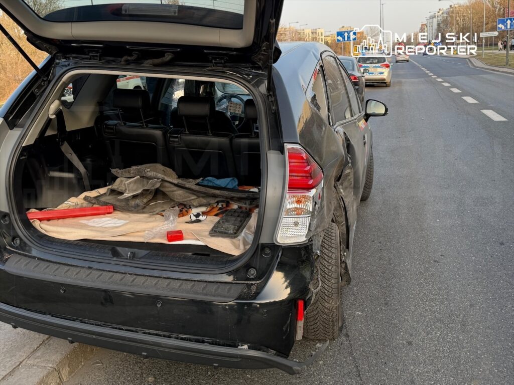 Czarny SUV z otwartym bagażnikiem, w którym leżą narzędzia i koc, zaparkowany na ulicy.