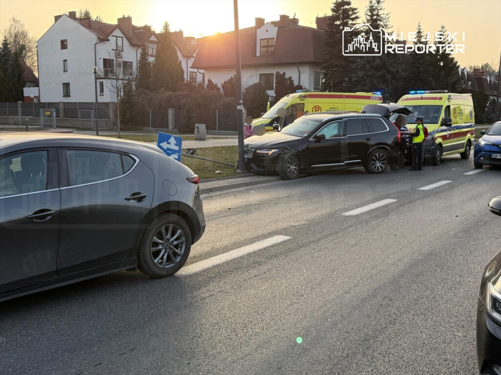 Na drodze doszło do kolizji, w której uczestniczyły dwa samochody; obok stoją karetki i policja.