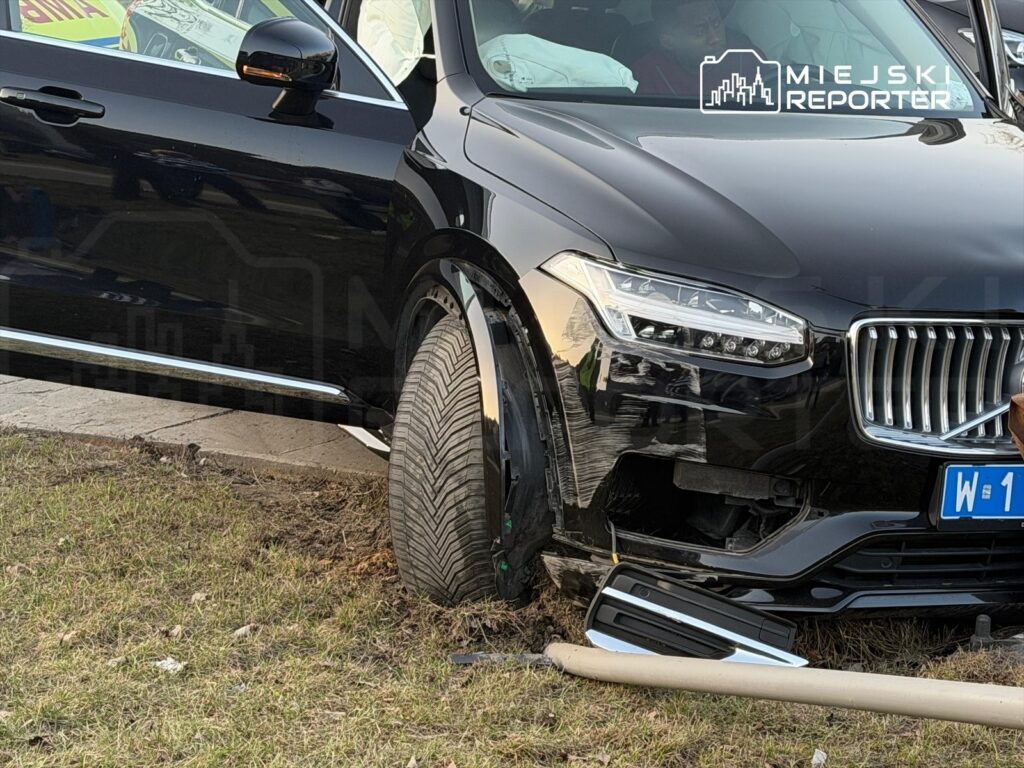 Czarny samochód osobowy z uszkodzoną oponą stoi na trawie obok drogi, z otwartymi drzwiami.