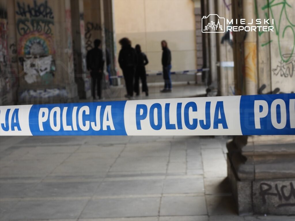 Policja zabezpiecza miejsce zdarzenia, wyznaczając strefę z niebieską taśmą w graffiti pokrytym przejściu.