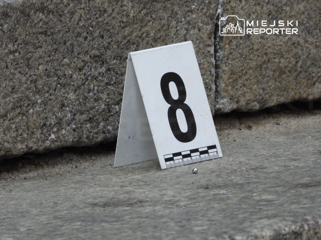 Numer 8 na białym znaku leży obok małego metalowego przedmiotu na szarej nawierzchni.