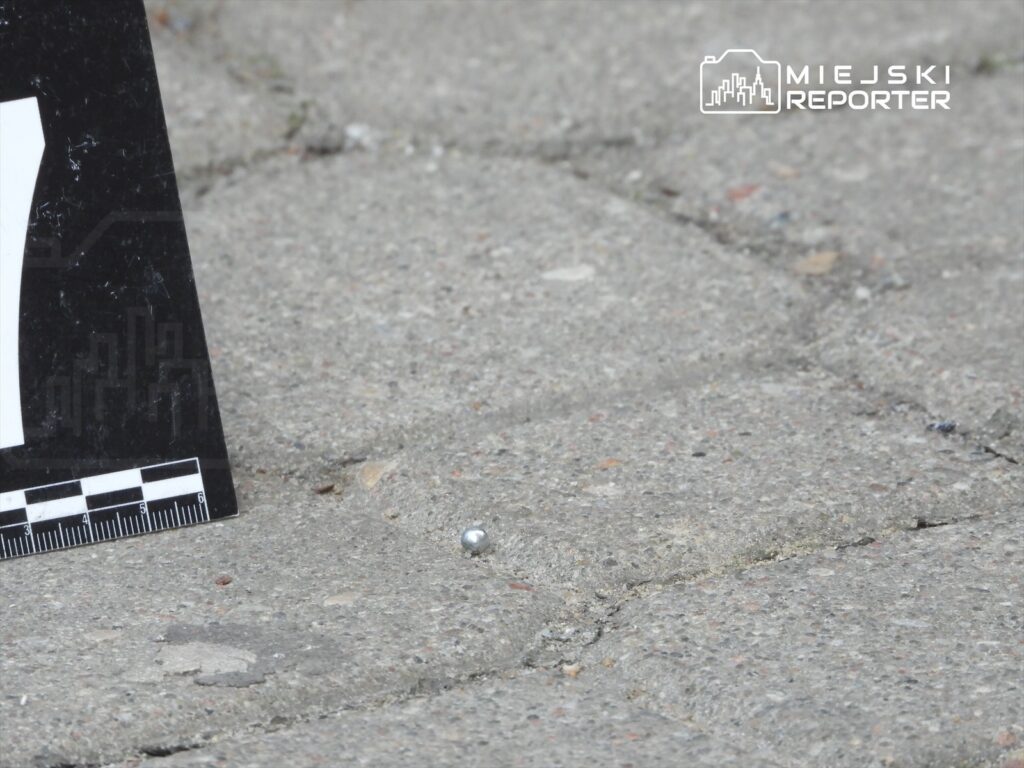 Srebrna kulka leżąca na bruku obok oznaczenia z numerem i skalą pomiarową.