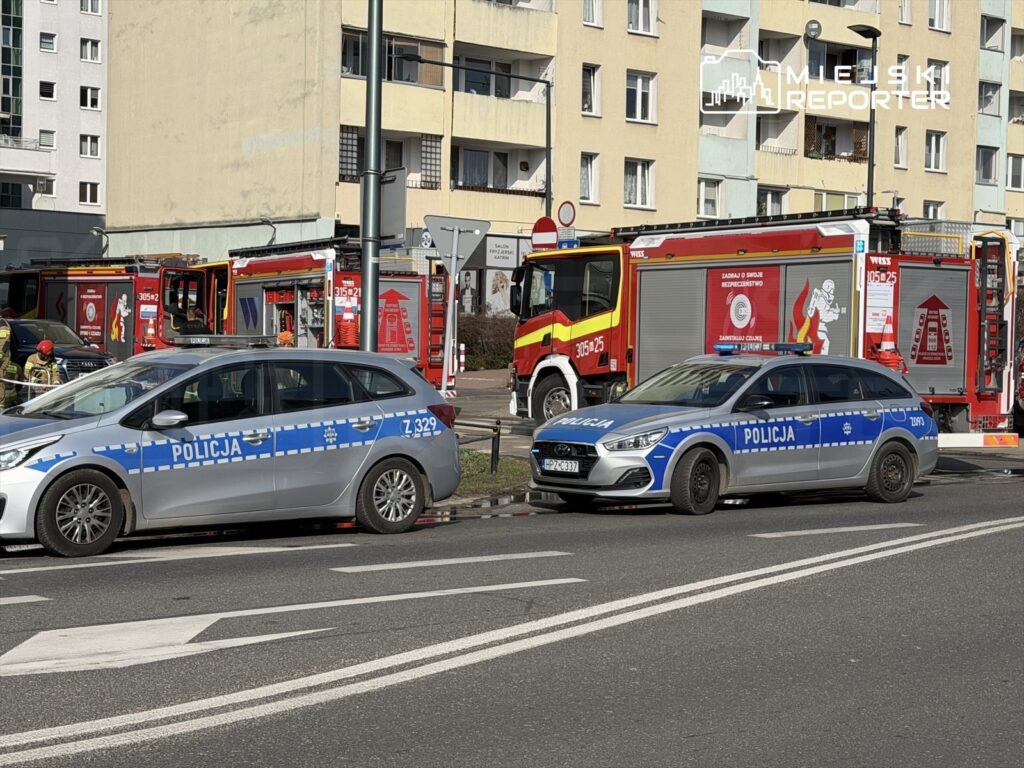Dwa radiowozy policyjne zaparkowane obok wozów strażackich w miejskim otoczeniu.