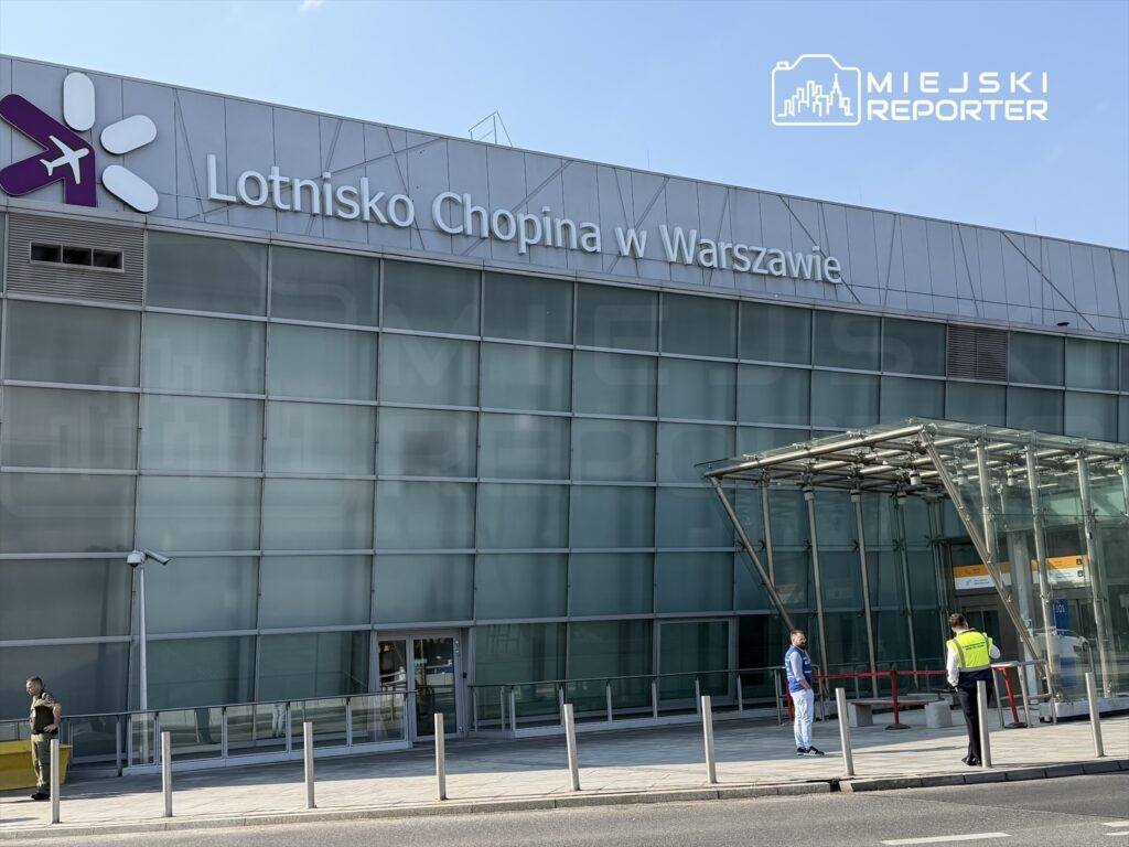 Lotnisko Chopina w Warszawie z przeszkloną fasadą, przy wejściu dwóch mężczyzn w mundurach rozmawia z osobą w niebieskiej kamizelce.