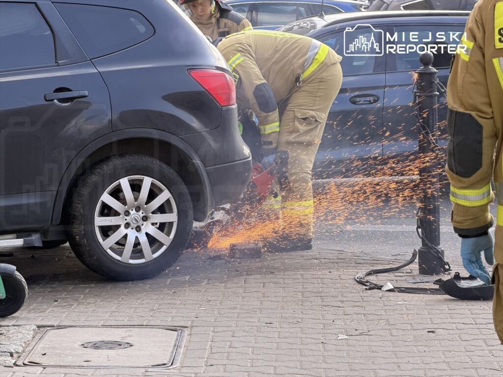 Strażak używający narzędzia tnącego przy czarnym samochodzie, generując iskry na ulicy.