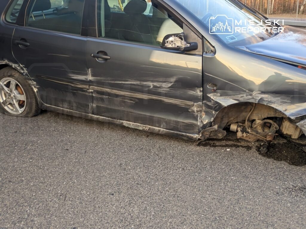 Uszkodzony samochód osobowy z wgniecioną karoserią i brakiem przedniego koła zaparkowany na jezdni.