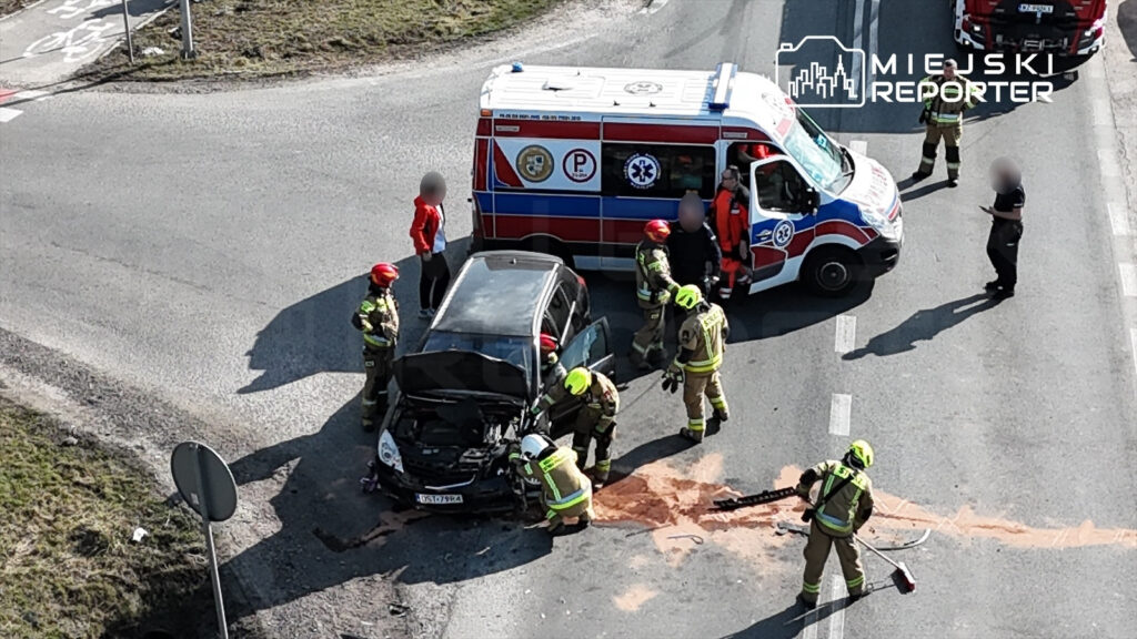 Na skrzyżowaniu zatrzymane są służby ratunkowe, które udzielają pomocy poszkodowanym w wypadku drogowym.
