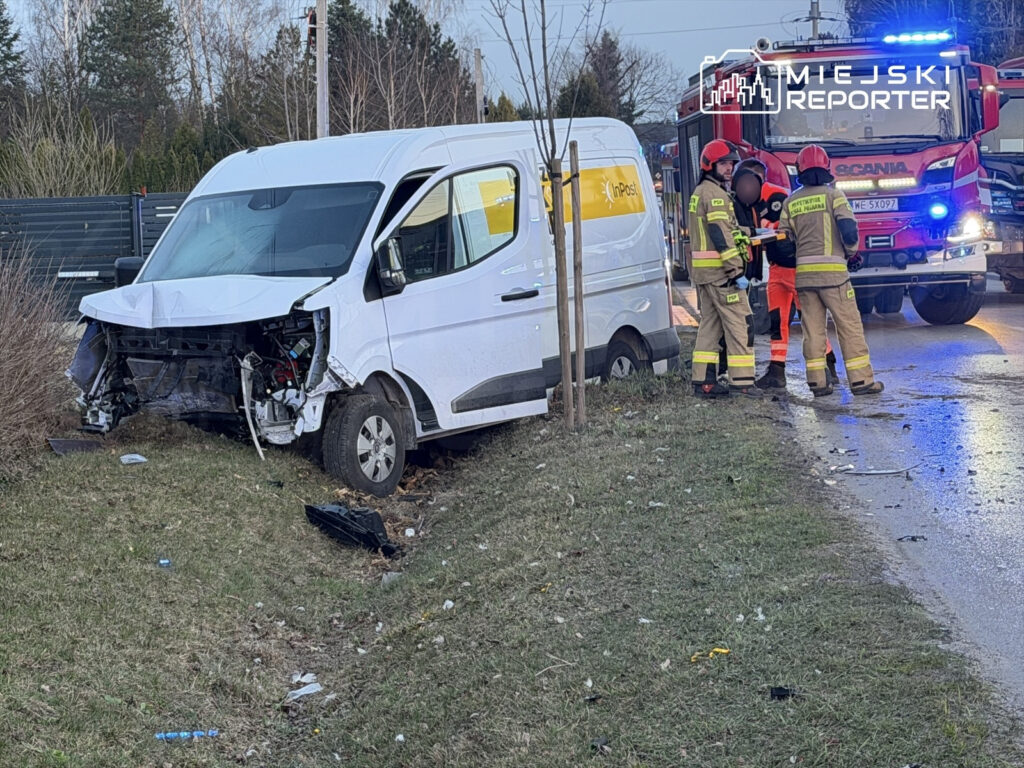 Biały furgon z uszkodzoną przednią częścią stoi na poboczu, obok ratownicy medyczni udzielają pomocy poszkodowanemu.