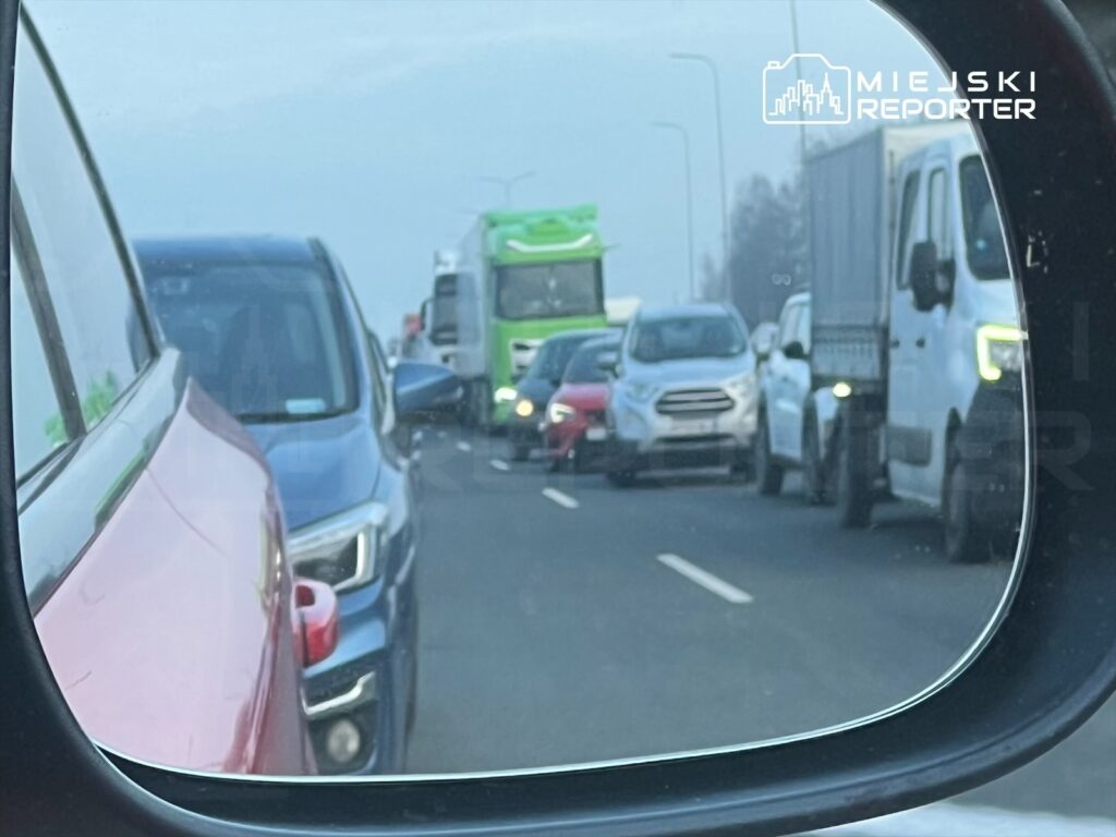 Ruch samochodowy w korku widoczny w lusterku wstecznym, z różnymi pojazdami na drodze.