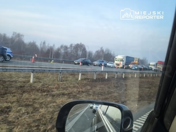 Ruch samochodowy na autostradzie z widocznymi pojazdami stojącymi w korku oraz oznakowaniem drogowym.