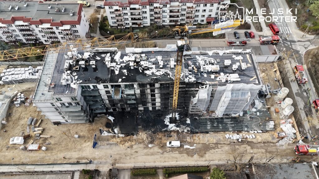 Trwają prace budowlane nad nowym obiektem mieszkalnym, z widocznym dźwigiem i materiałami budowlanymi na placu.