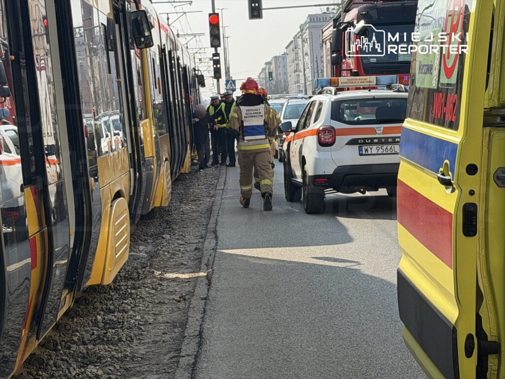 Służby ratunkowe interweniują przy tramwaju zatrzymanym na ulicy, obok stojące pojazdy i sygnalizacja świetlna.